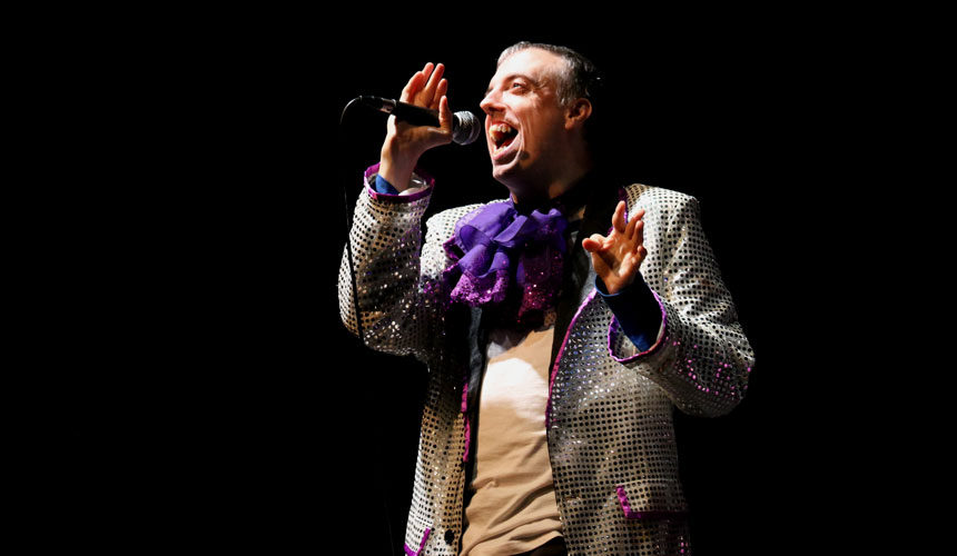 A man in a sequin suit jacket talking into a microphone