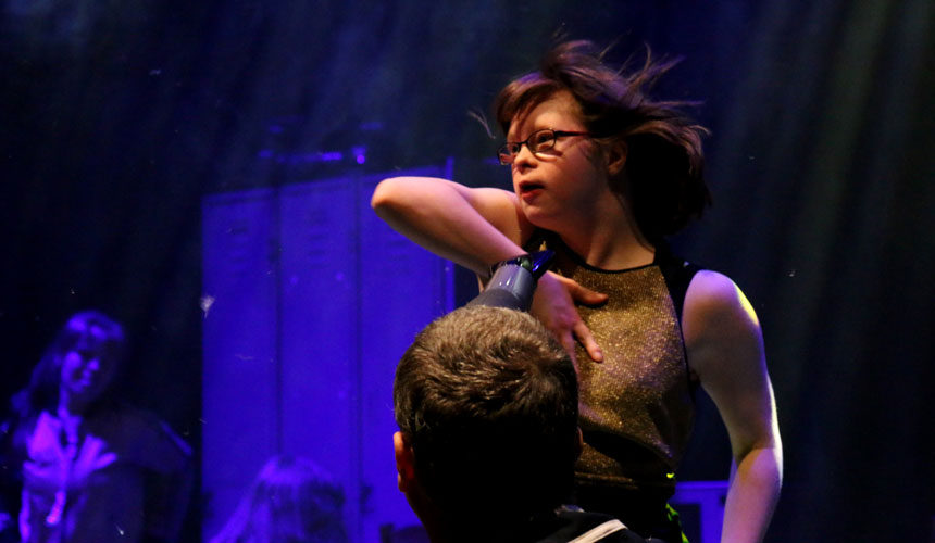 A woman dancing. A man is in front of her using a hairdryer on her face.