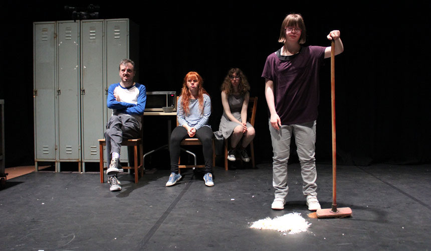 A woman stands with a broom and a pile of popcorn. Three people are sat in the background.