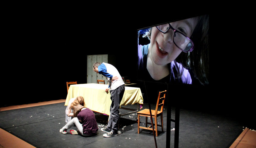 An woman looking into a camera is on a tv screen. In the background you can see the woman being filmed.