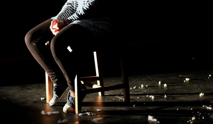 A woman sat on a chair, you can only see form the waist down. The floor is covered in popcorn and feathers.