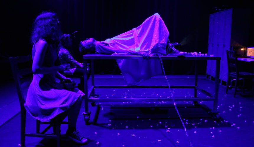 Two women from the side. In between them is a man on a table covered in a white cloth from the chest down.