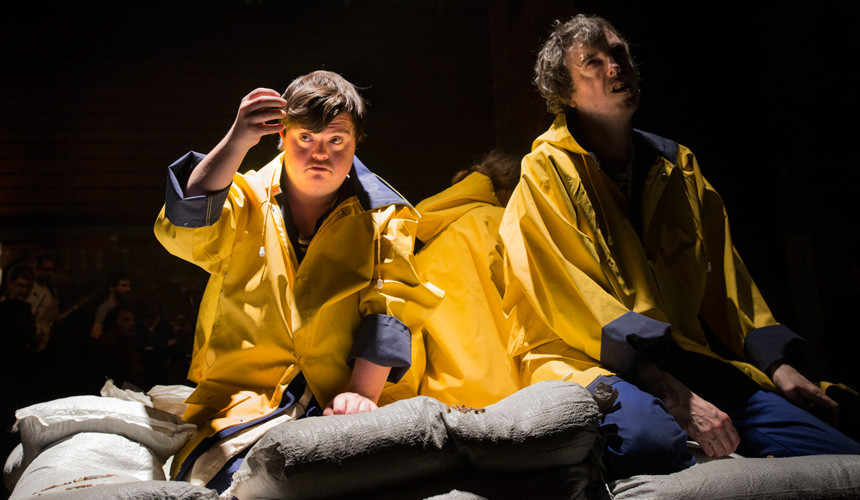 Two men in yellow raincoats look disheartened surrounded by sandbags.